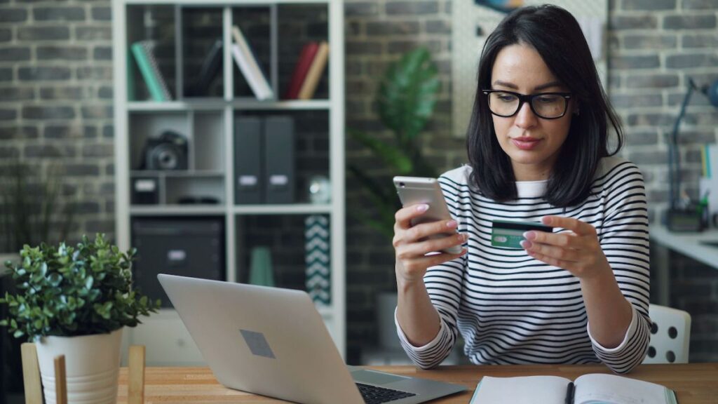 Persona utilizando una tarjeta de crédito y revisando información financiera en su celular
